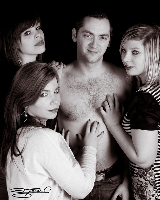 A man posing shirtless with three women who have their hands all over him