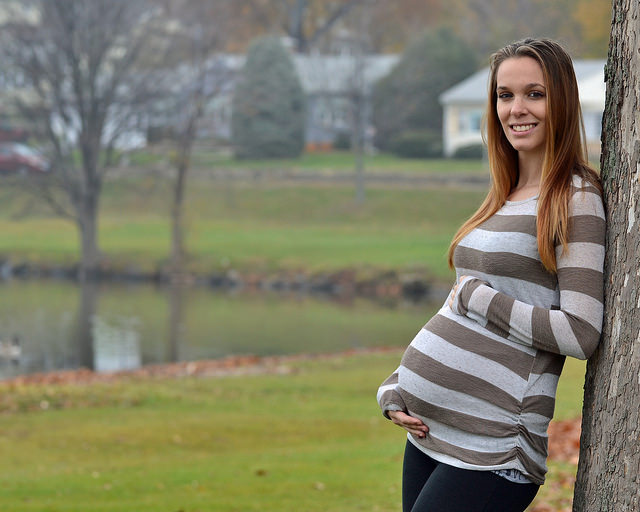 A pregnant woman holding her stomach while standing next to a tree