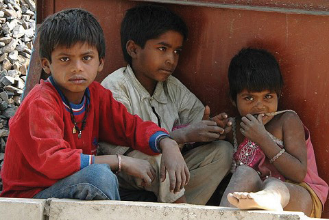 Three poor kids sitting in the shade on the street