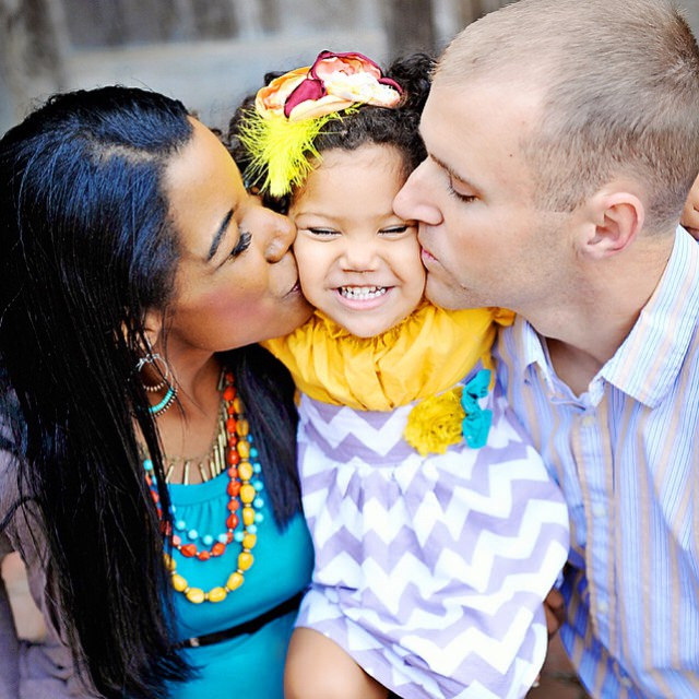 A white man and a black woman kissing their daughter