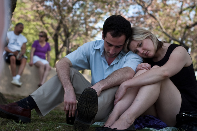 Two couples in a park. One sitting on a rock, and one resting against each other on the ground