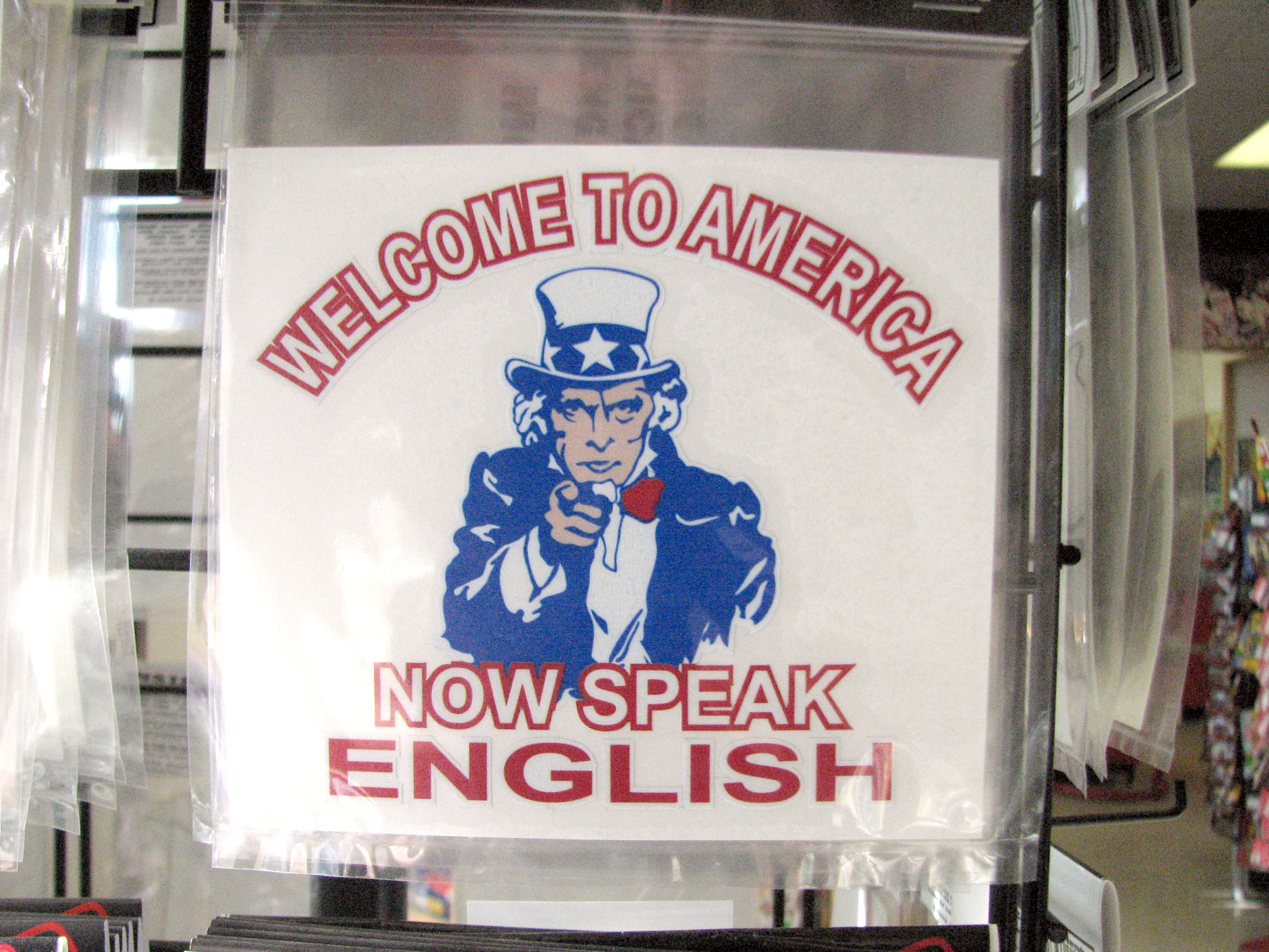 A sticker in an American gift shop that reads welcome to America, now speak ENGLISH!