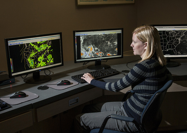 Woman sitting at a desk with many computer monitors