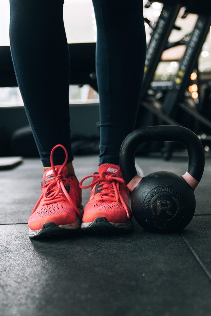 Legs and feet in red tennis shoes with a kettlebell sitting next to them.