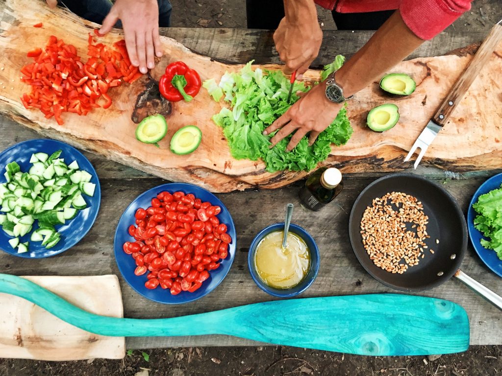 A variety of colorful fresh food being chopped and prepared for a salad (lettuce, tomatoes, red peppers).