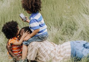 Parent and kids laying on the ground. One child is looking at a cell phone.