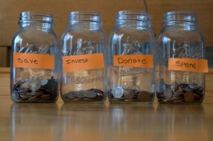 Glass jars filled with coins and marked Save, Invest, Donate, and Spend.