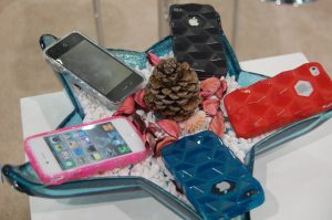 Smartphones sitting on a star-shaped display featuring a pine cone, leaves, and rocks.