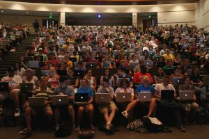Students in a lecture hall with laptops, mainly Mac laptops.