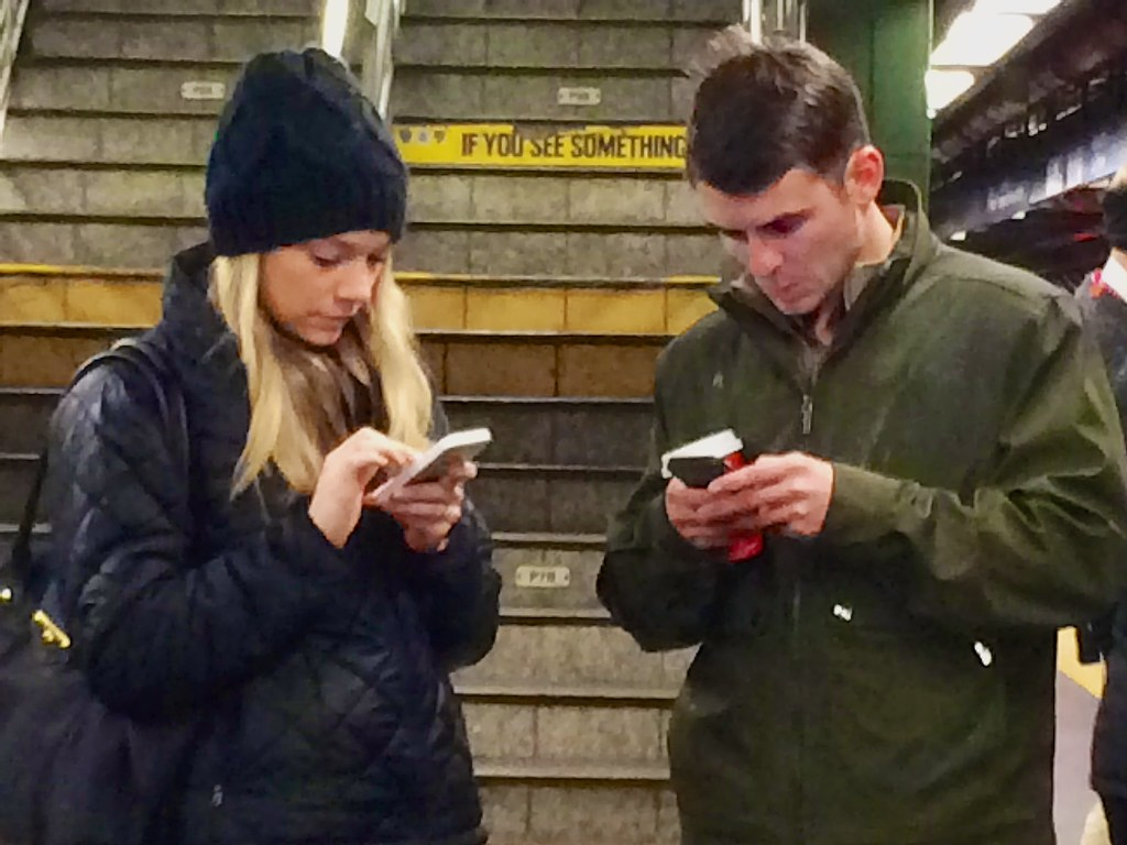 Two young adults looking at their cell phones.