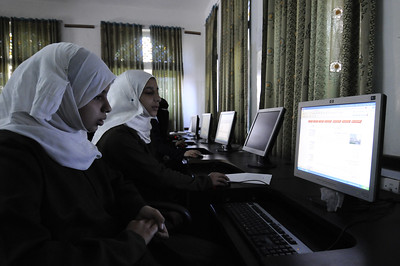 Young women in hijabs using desktop computers.