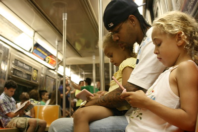 A child with her family using a cellphone on the subway.