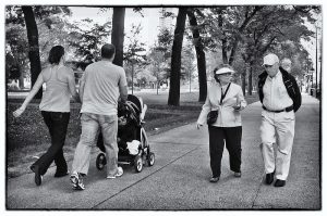 A couple with a child in a stroller passing by an elderly couple.