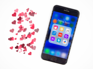 Mobile phone showing dating apps and many pink and red hearts around it.