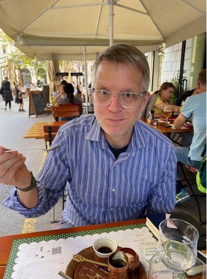A man wearing glasses and a blue pinstripe shirt sits at a table in front of coffee.