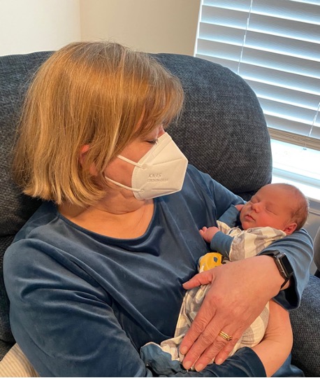 Seated blonde woman wearing a white N95 mask holding an infant