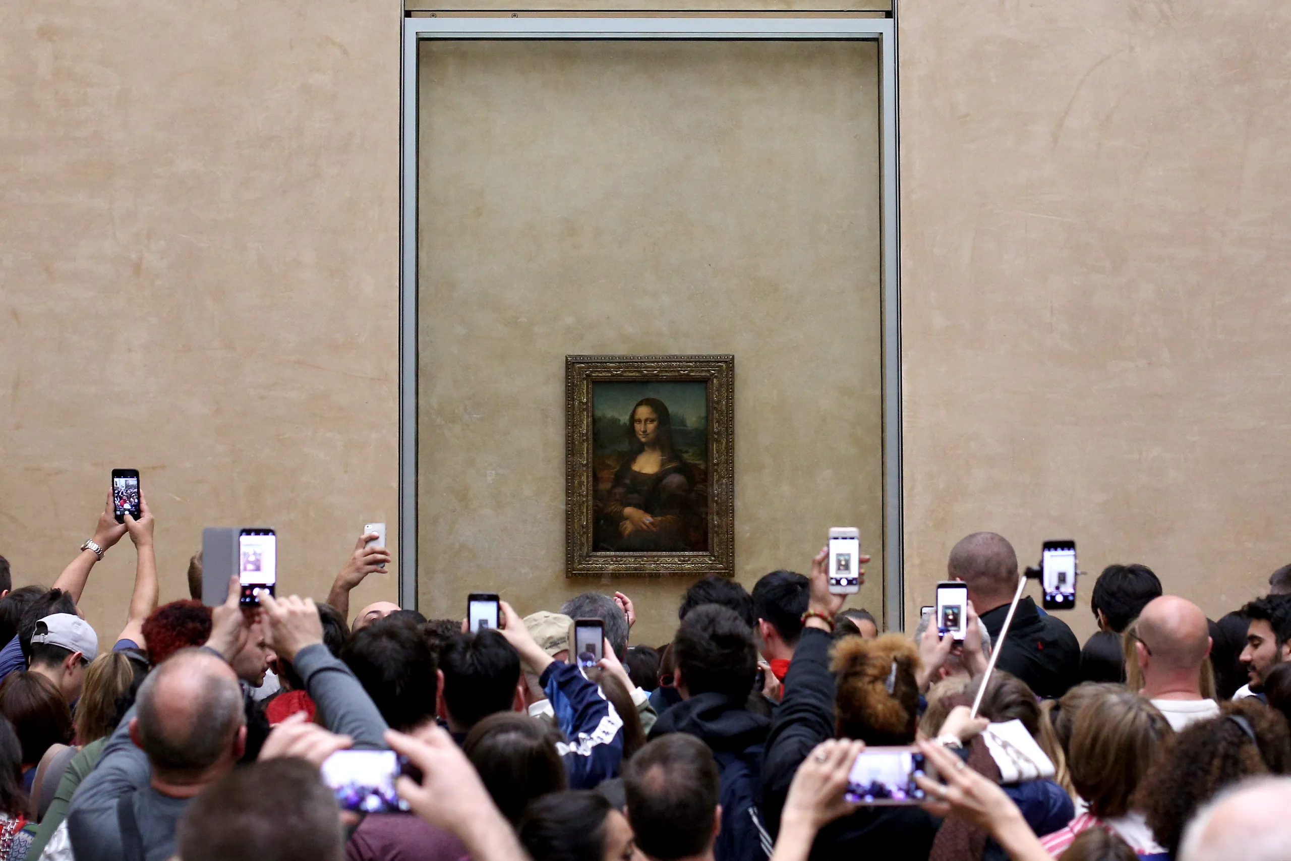 Image of a crowd of people in front of the Mona Lisa painting; many of them are taking pictures with their phones.