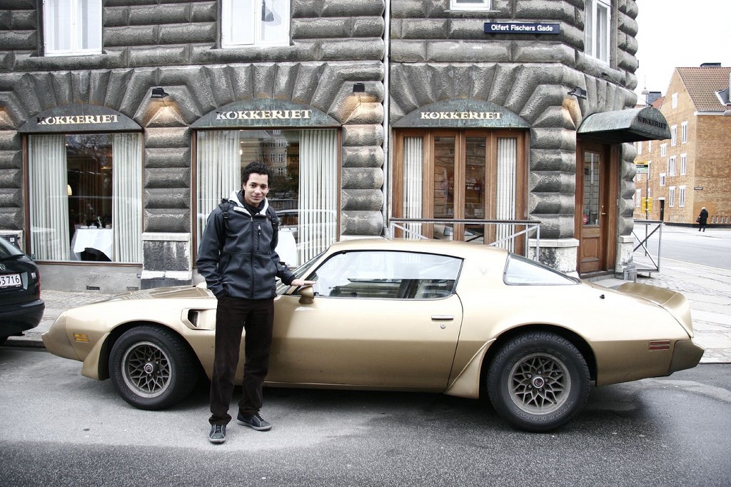 A young man standing next to an old sports car